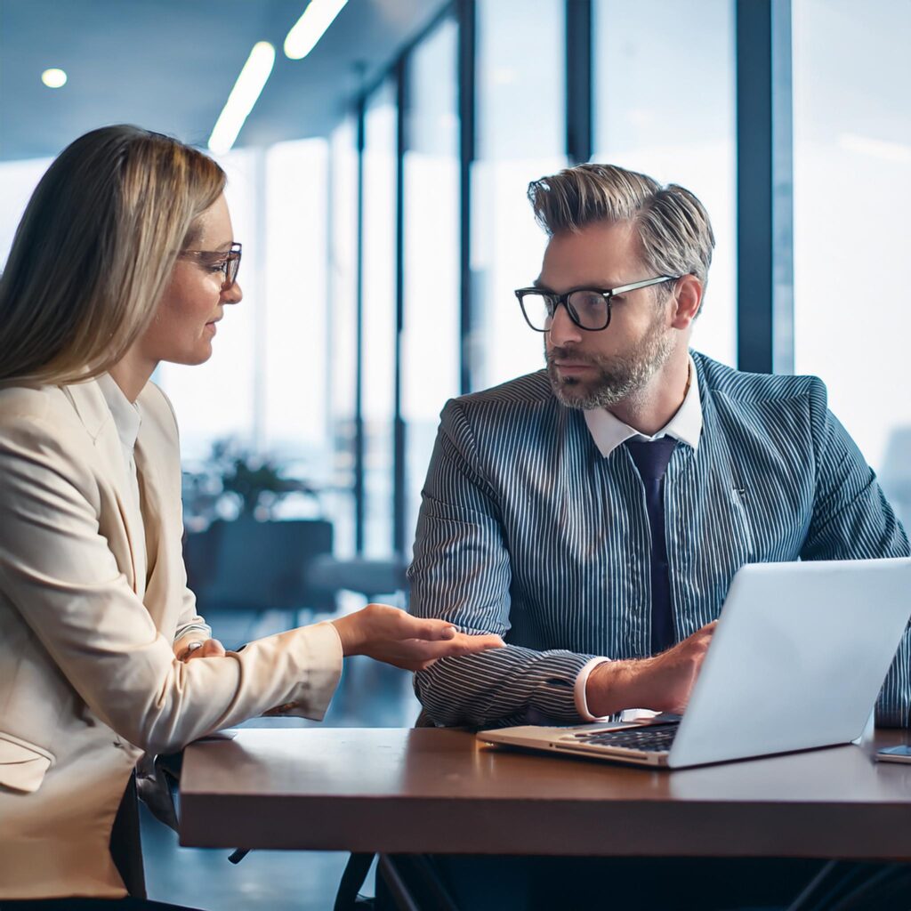 2 Menschen unterhalten sich an einem Schreibtisch in einem hellen Büro